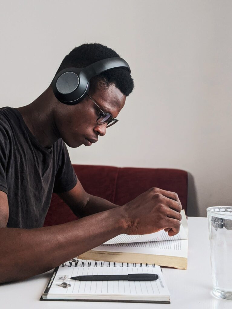 Man Wearing Black Crew-neck T-shirt Using Black Headphones Reading Book While Sitting